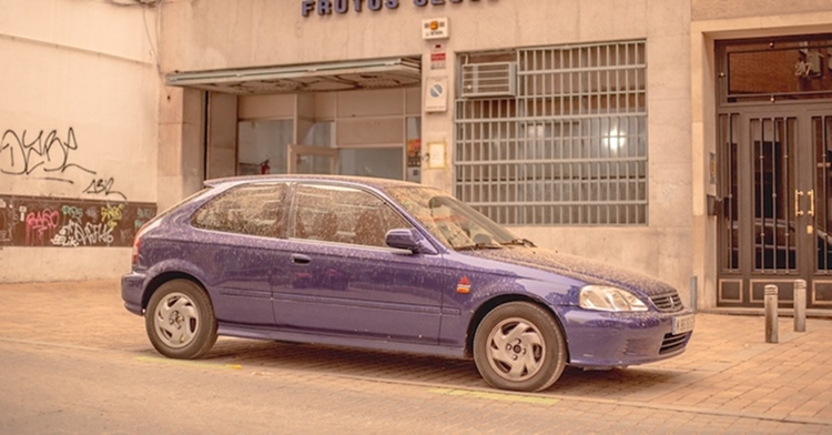 Coche morado cubierto de polvo aparcado en la calle